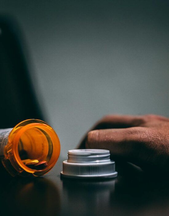 Moodily lit scene of an open prescription bottle and hand on a table, depicting healthcare themes.